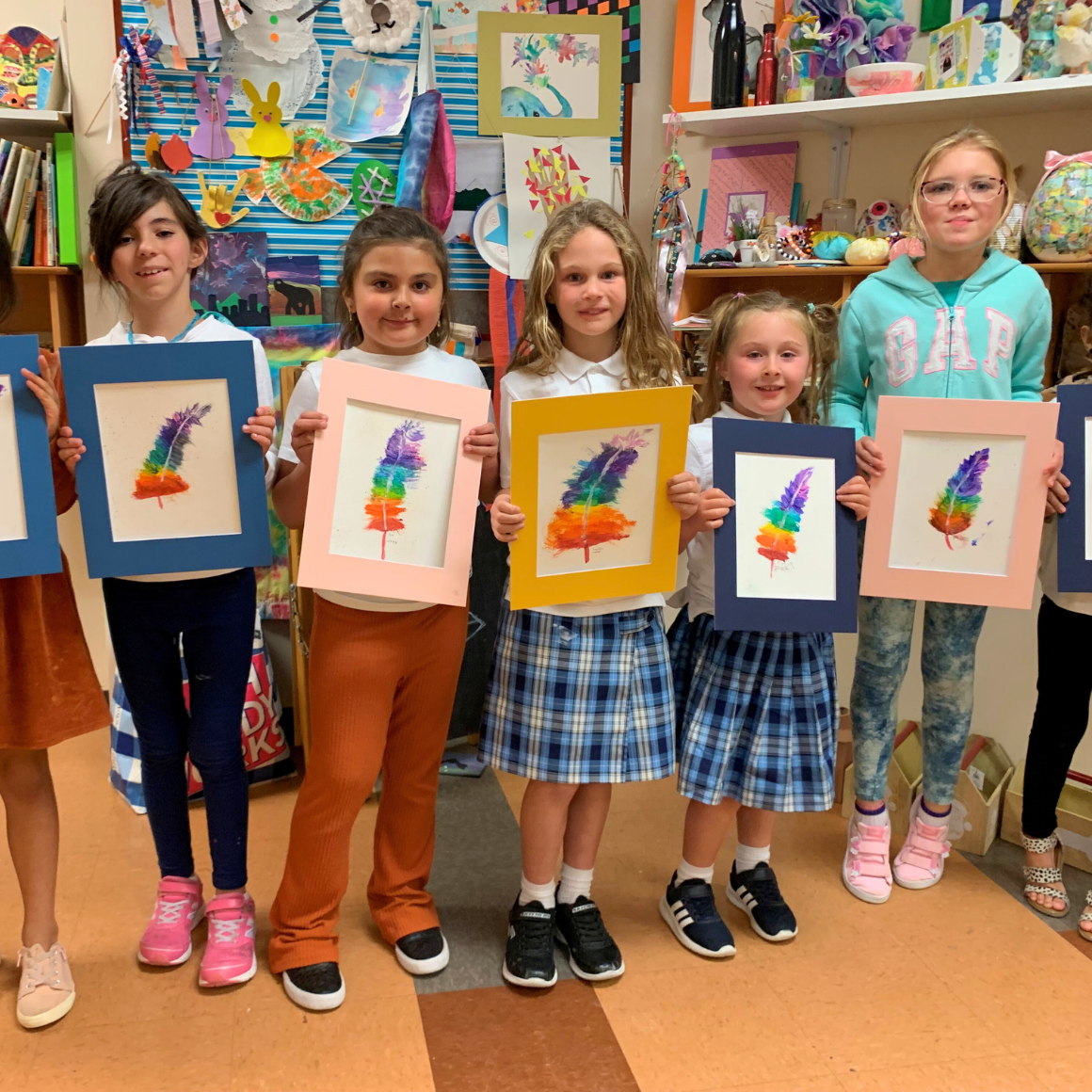 Trails Art and Craft Department | Kid in an arts class holding up watercolor feather paintings.