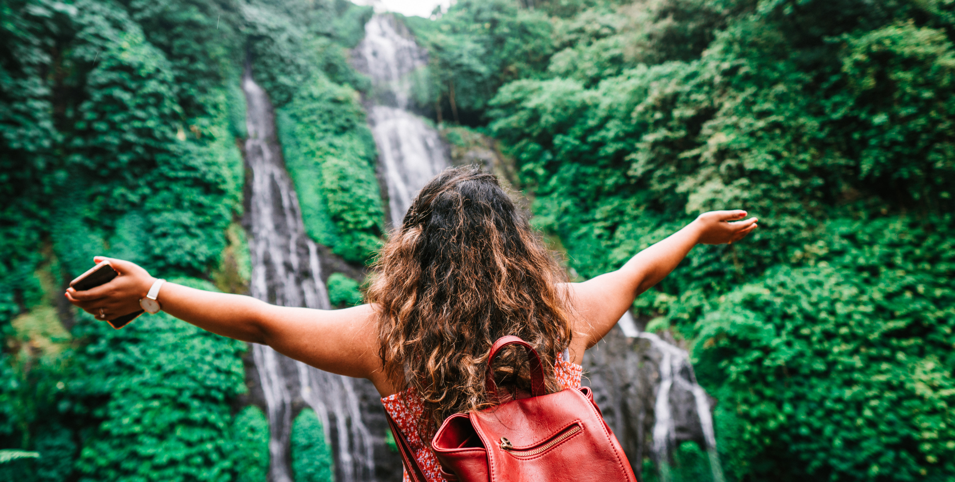 Special Interest Travel Header | woman with arms outstretched in front of a waterfall in a jungle