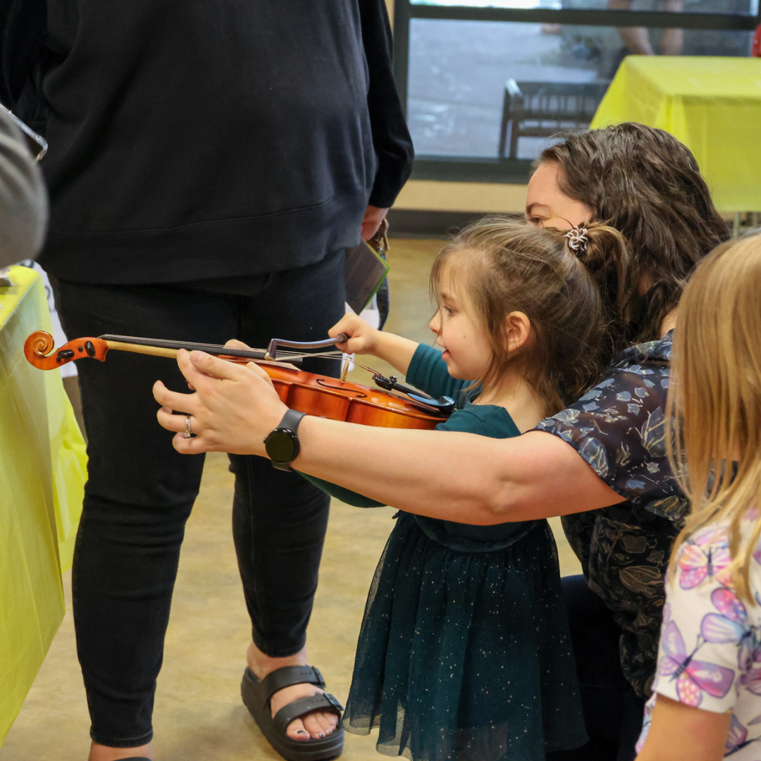 Health Fair 2024 | Teacher helping a young child play the violin