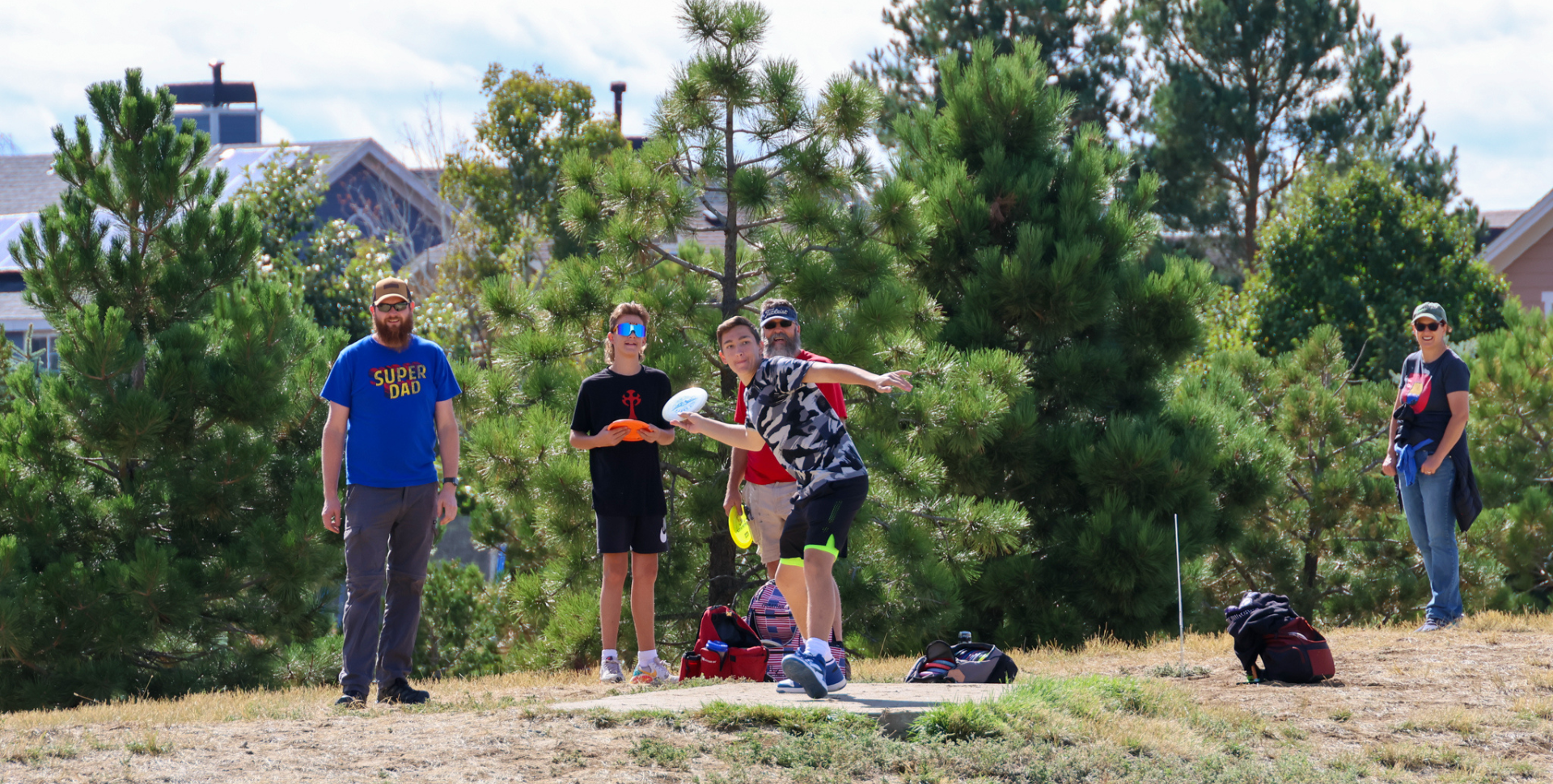 Youth Disc Golf Header | a male youth on a hill about to throw a disc frisbee toward a basket